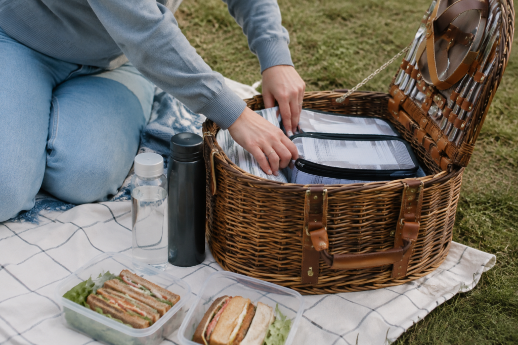 Open picnic basket on a grass blanket with sandwiches in reusable containers