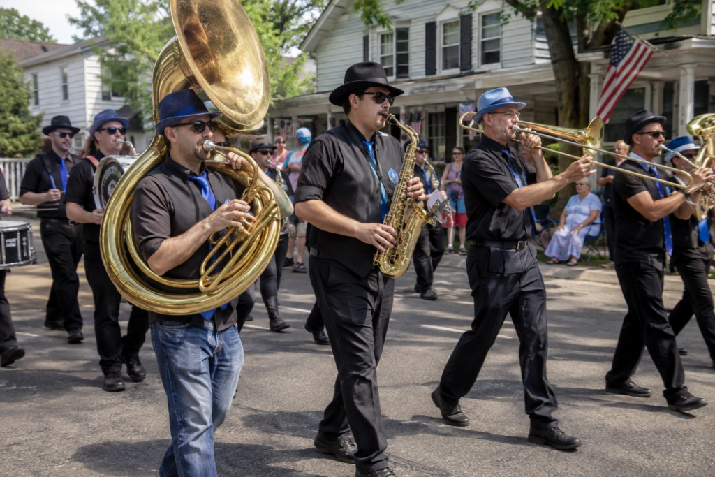 Brass marching-band instruments and neatly coordinated adult parade musicians seen from the side walking along a generic small-town street