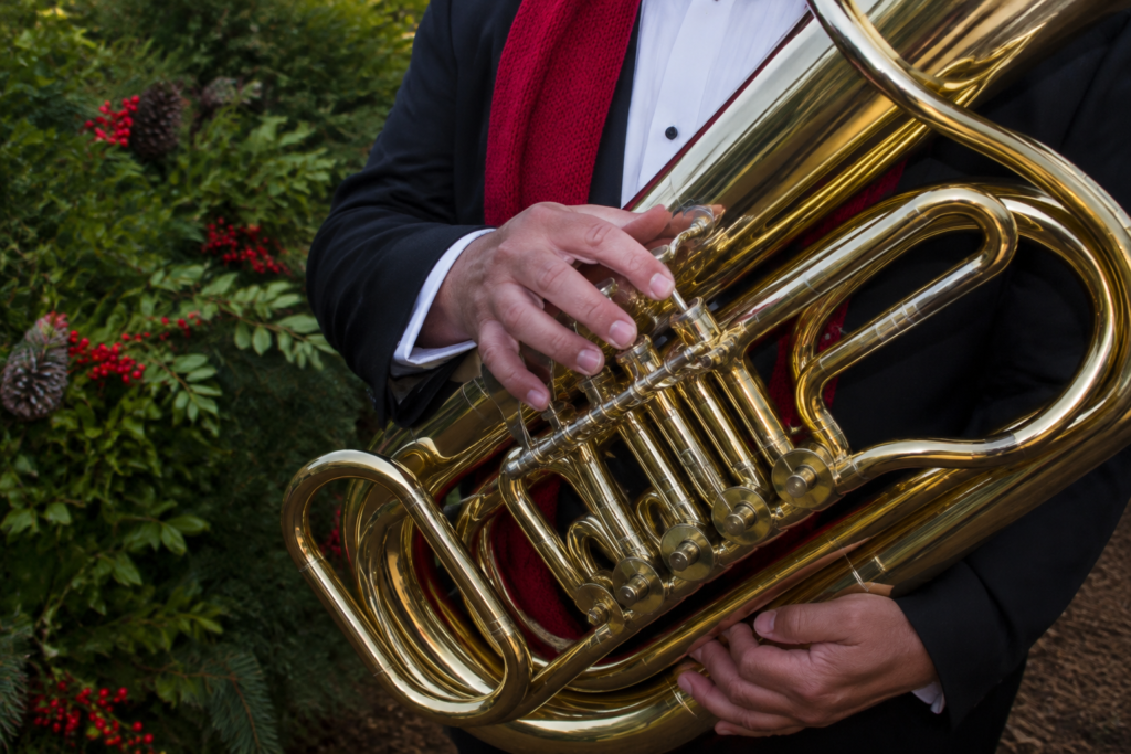 A tuba player holding a gleaming brass instrument with festive red scarf visible