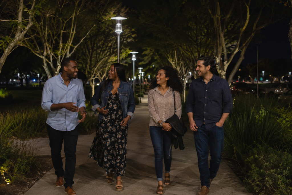 Friends walking together along a tree-lined pedestrian path after an outdoor performance at night