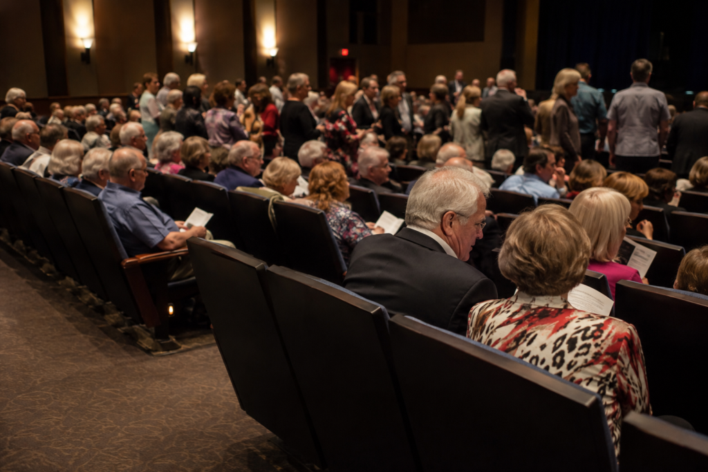 Elegant indoor performing arts audience settling into plush dark seats before a show