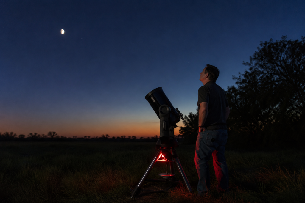 Amateur astronomer standing beside a realistic small reflector telescope in a dark park clearing