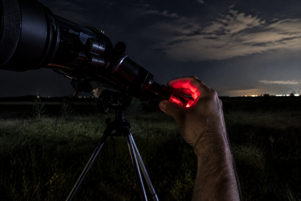 Close view of a hand adjusting a real telescope eyepiece with a dim red flashlight