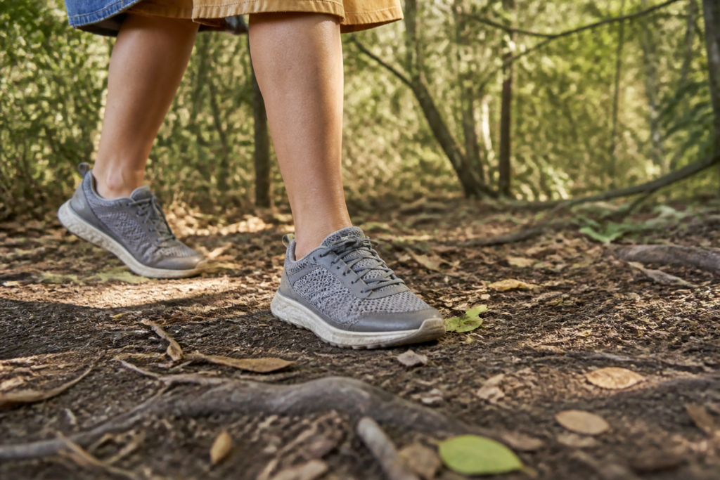 Close low angle of comfortable walking shoes and short unobstructive costume hems moving along a mulched woodland path