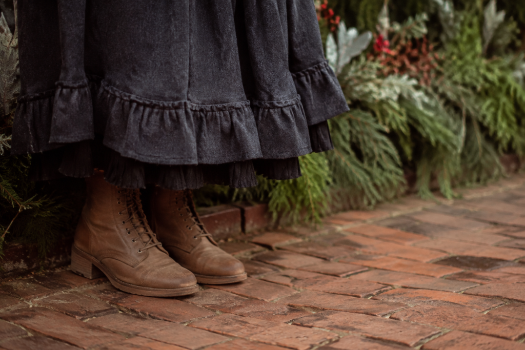 Detailed close-up of sturdy walking boots beneath a Victorian-inspired long wool skirt beside a vintage brick sidewalk