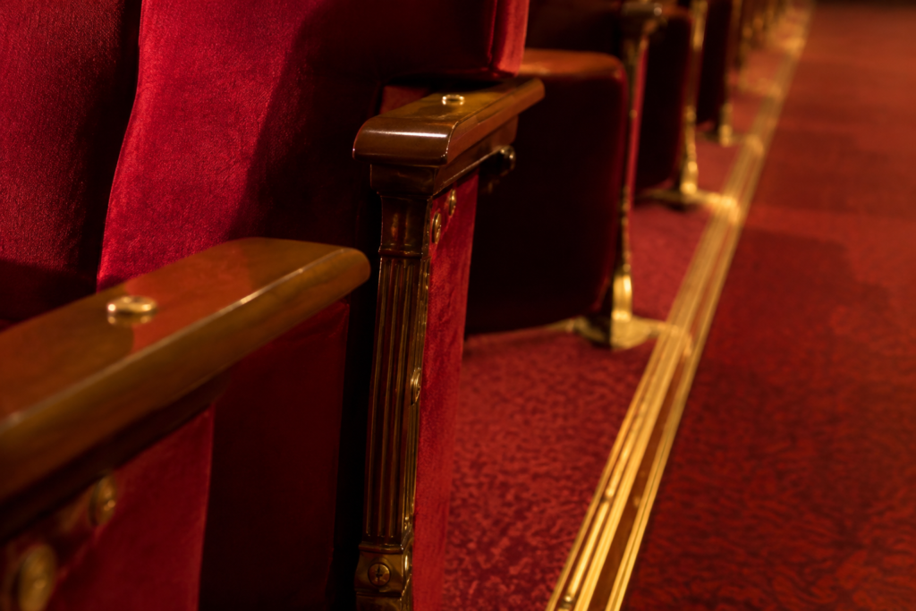 Close detail of elegant red upholstered theatre chairs and brass aisle trim under warm house lights